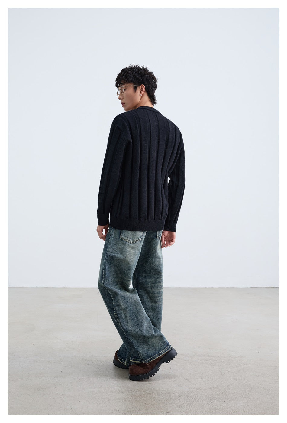Rear view of a model wearing a black ribbed sweater with jeans.