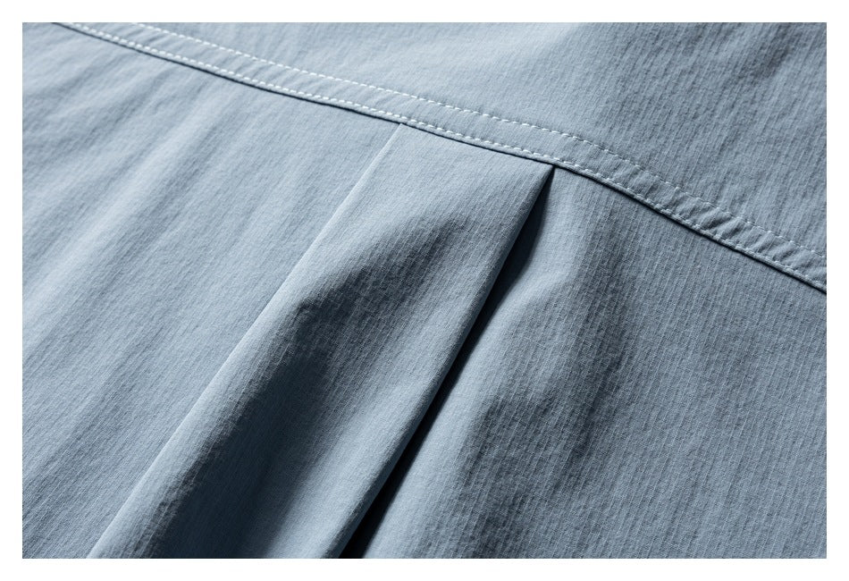 Close-up of blue-gray garment fabric showing a stitched seam and folded pleat.
