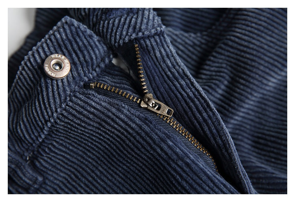Close-up of navy ribbed trousers showing the metal zipper and waistband button.
