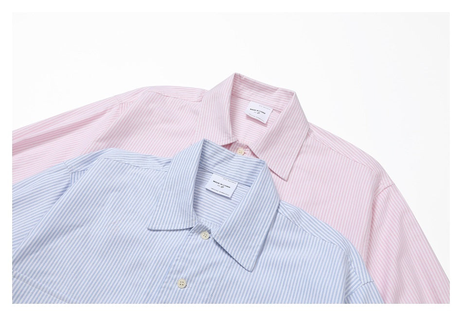 Close-up of overlapping pink and light blue pinstriped shirts, showing their collars and buttons.