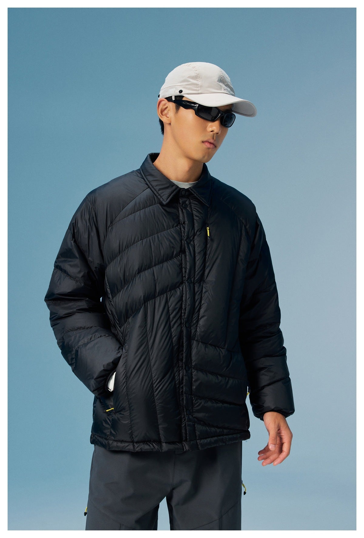 Model wearing a black quilted snap-front jacket with a pointed collar and yellow zipper accents.