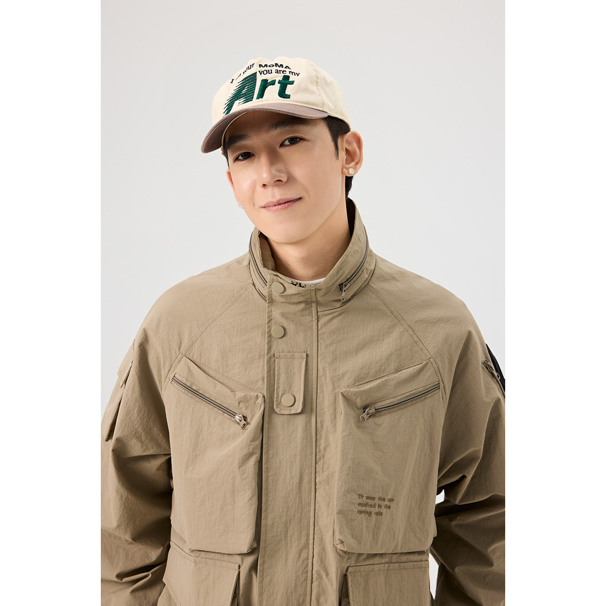 Close-up of a model wearing a khaki utility jacket with a high collar, snap placket, and two zip chest pockets.