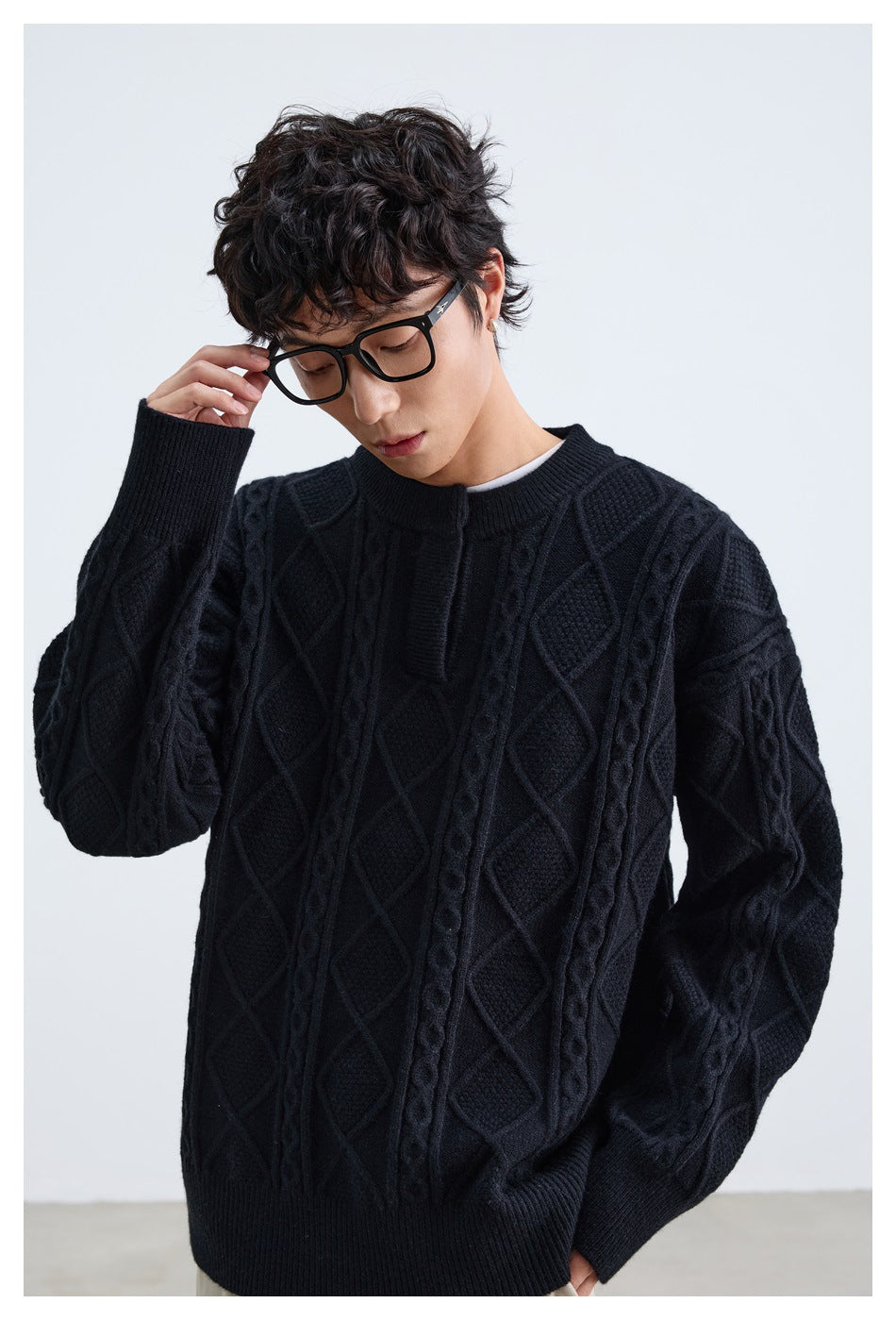 Model wearing a black cable-knit sweater with diamond patterns and ribbed cuffs and hem.