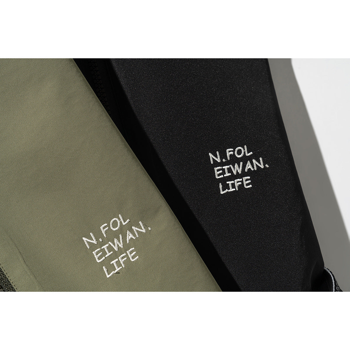 Close-up of white embroidered lettering on olive and black jacket fabric.