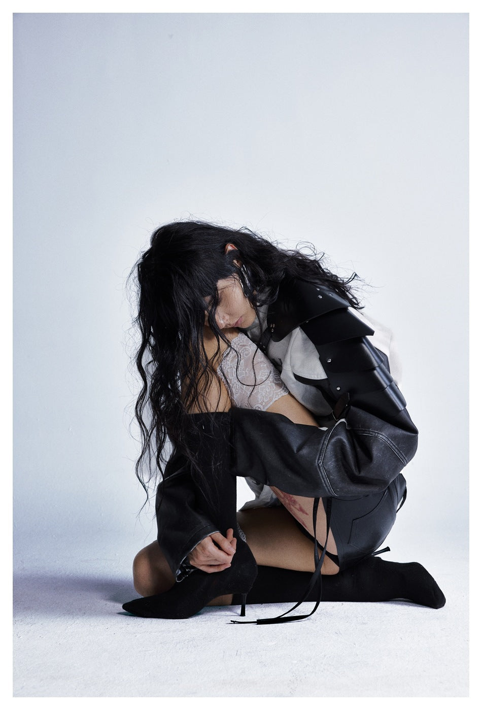 Model crouching in the off-white and black jacket, showing its layered black shoulder panels and long sleeves.