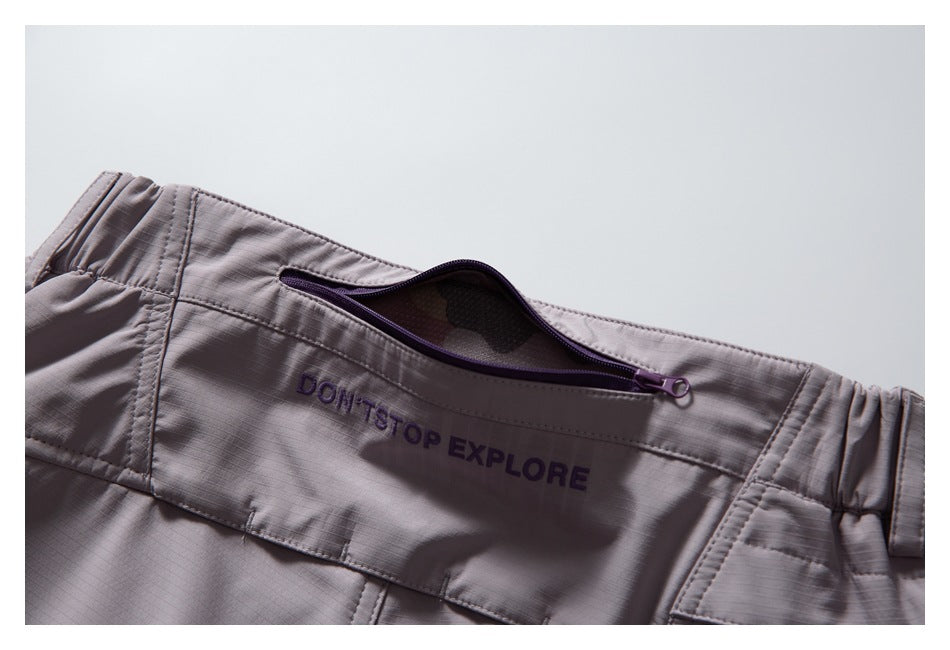 Pale mauve trouser waistband with an open purple zip pocket and embroidered “DON'T STOP EXPLORE” text.