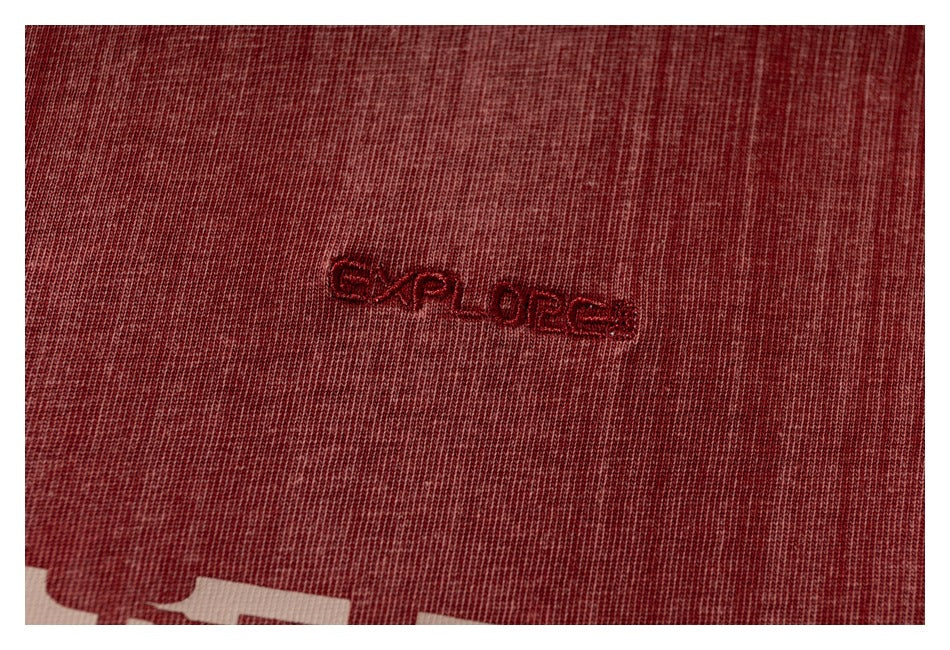Close-up of small dark red embroidered lettering on burgundy T-shirt fabric.