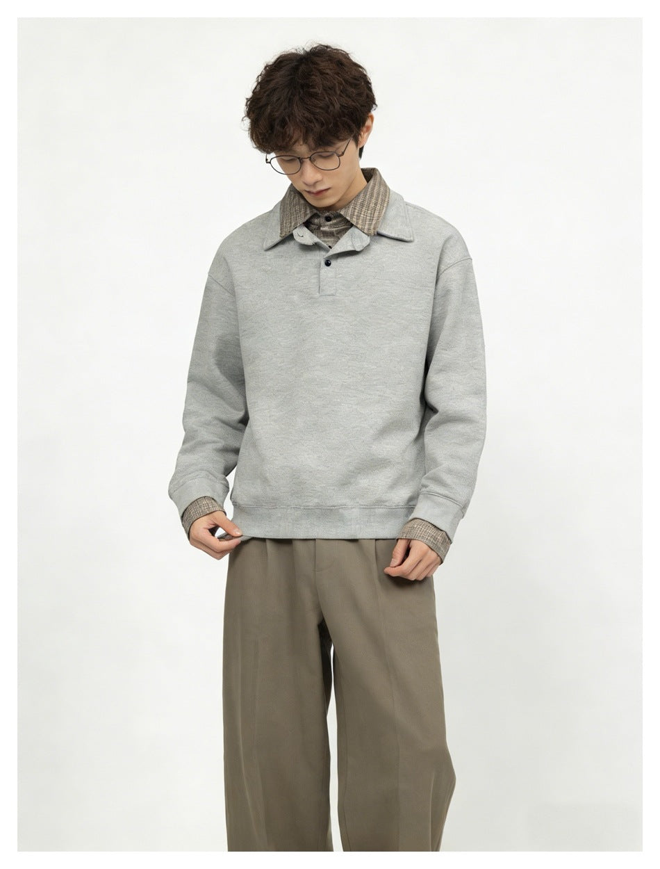 Model wearing gray layered-look sweatshirt with plaid collar and cuffs, with olive-brown trousers, front view