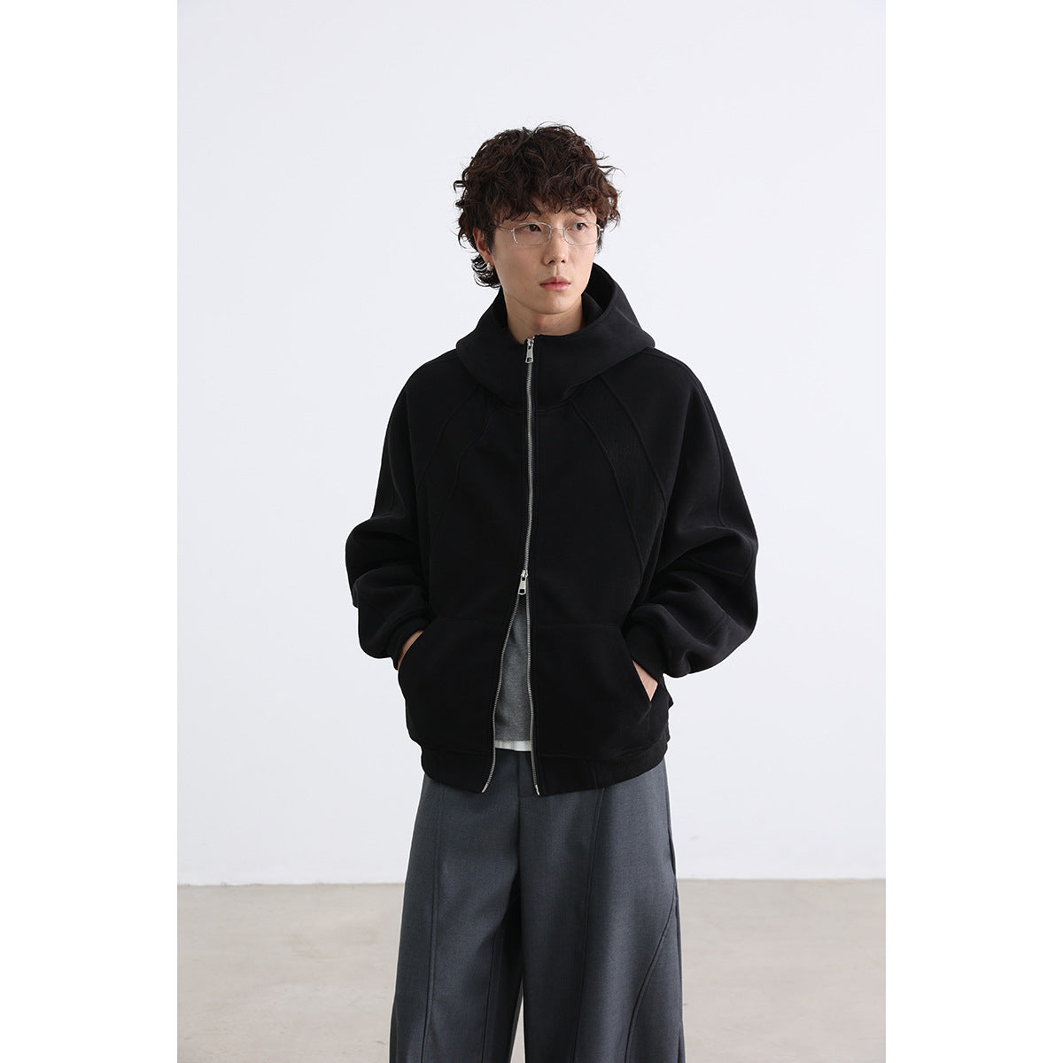 Model wearing a black zip-up hoodie with an oversized hood, raglan seams, and front pockets.