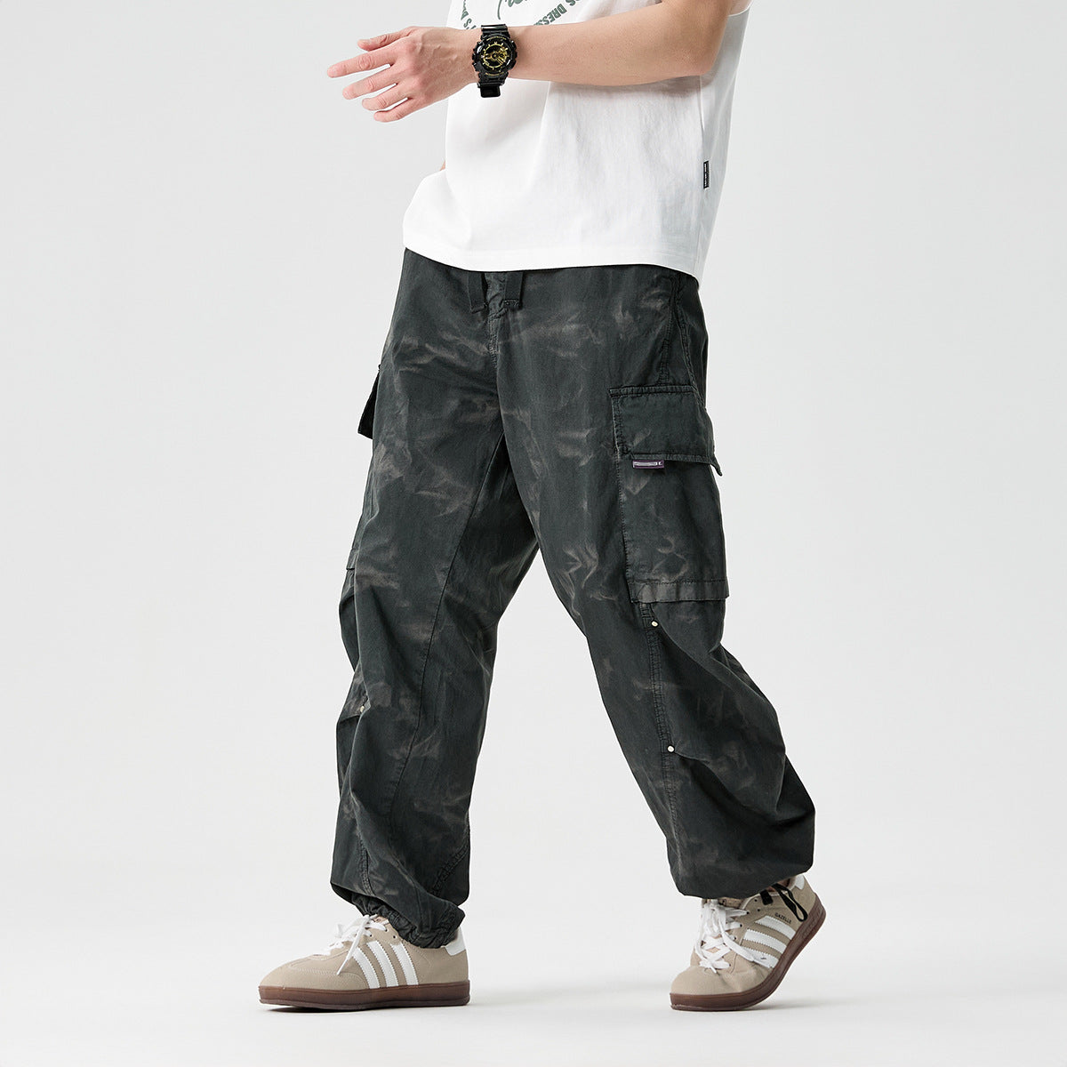 Cropped model wearing loose charcoal cargo pants with multiple flap pockets and gathered ankles, shown from the front.