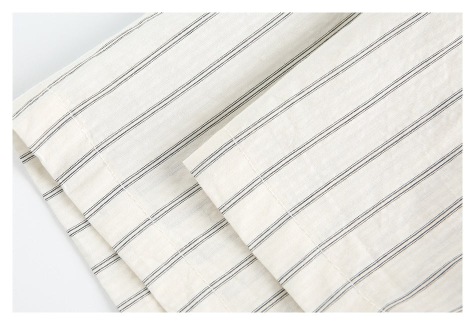 Close-up of overlapping striped ivory shirt fabric, showing a folded cuff or edge and stitching.