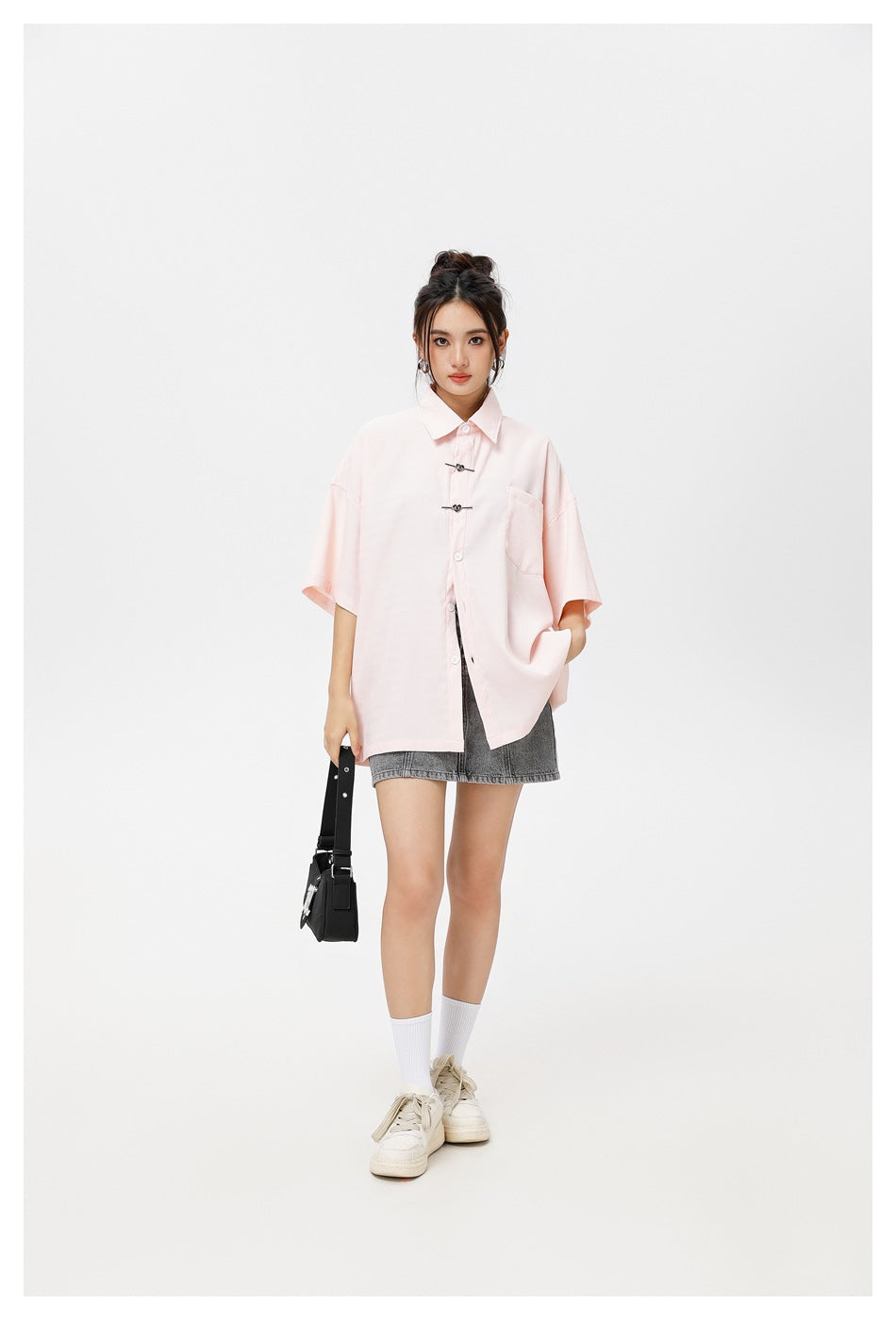 Model wearing a pale pink oversized short-sleeve button-up shirt with a chest pocket and decorative front clasps.