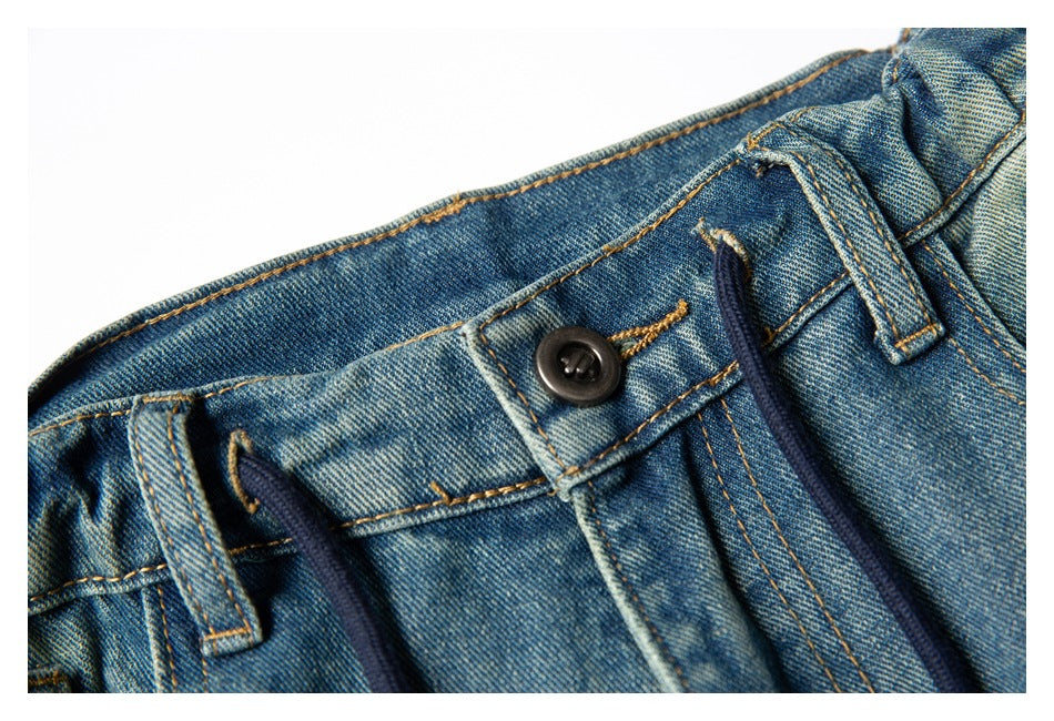 Close-up of the front waistband and button closure on blue denim trousers, with a dark drawcord and belt loops.