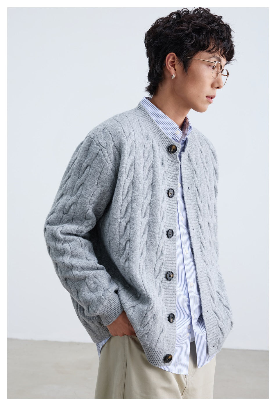 Angled front view of a person wearing a light gray cable-knit cardigan with dark buttons.