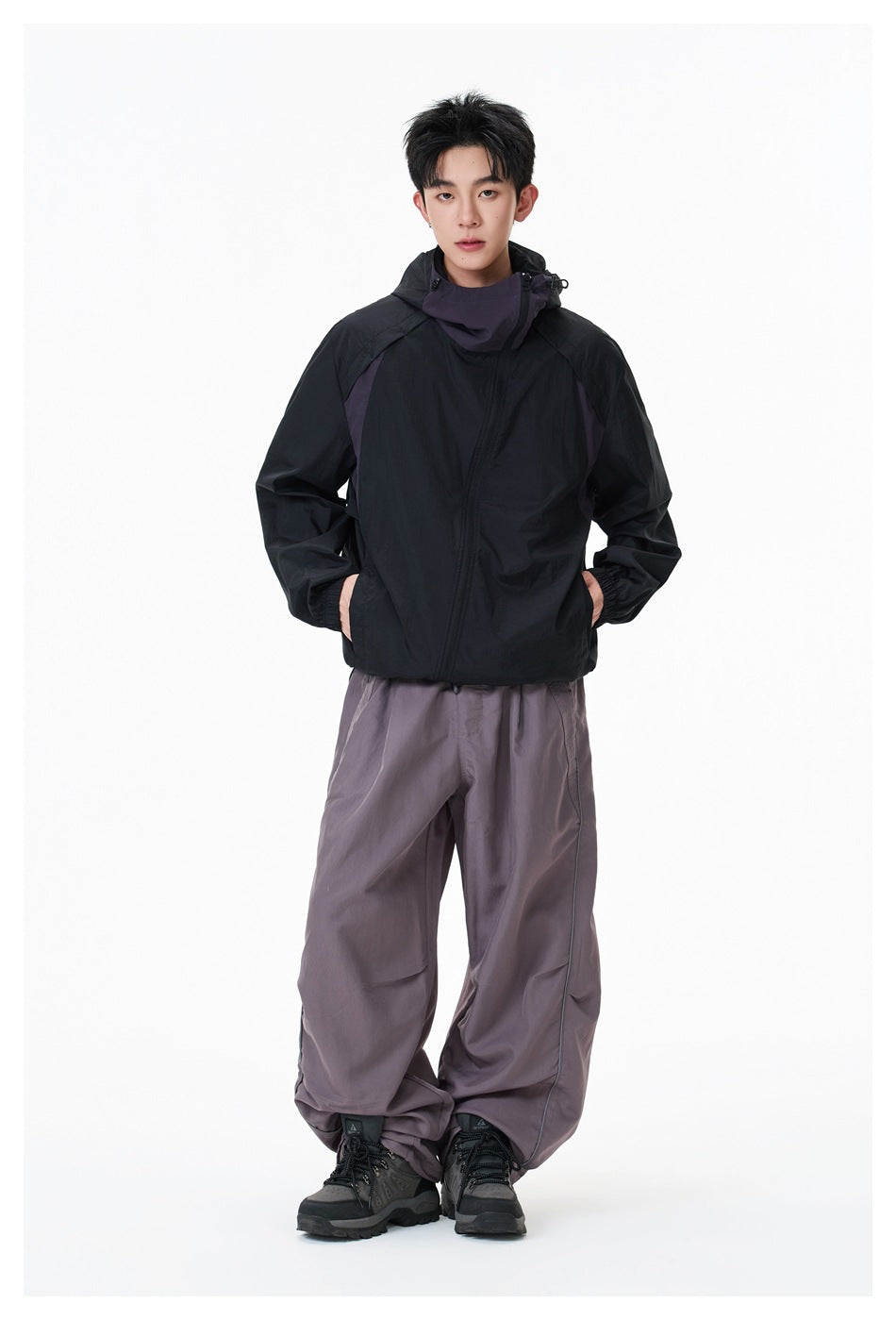 Full-length front view of a model wearing a black hooded jacket with purple-gray accents and loose gray-purple pants.