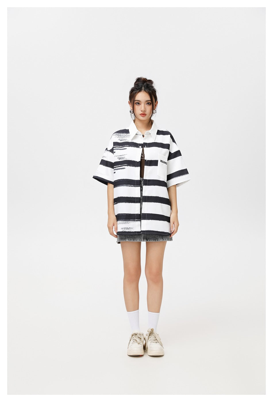 Model wearing an oversized black and white striped short-sleeve shirt open over a dark top with a gray denim skirt