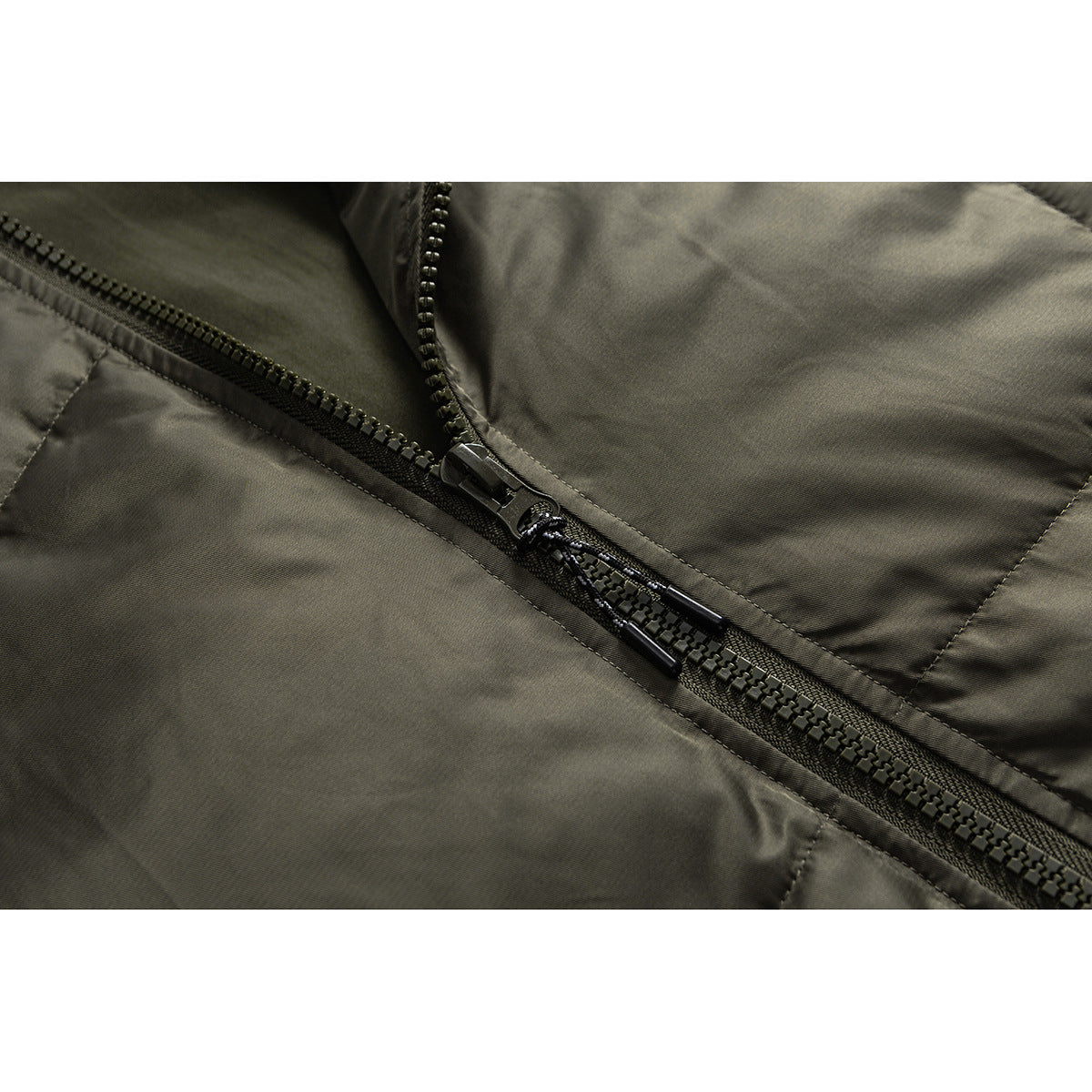 Close-up of an olive jacket's front zipper, metal teeth, pull cords, and stitched panels.