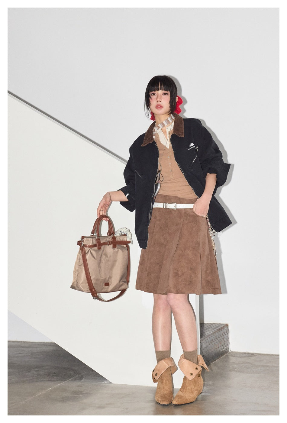 Model wearing an open dark navy jacket with a brown collar over a tan top, with a brown skirt and tan boots.