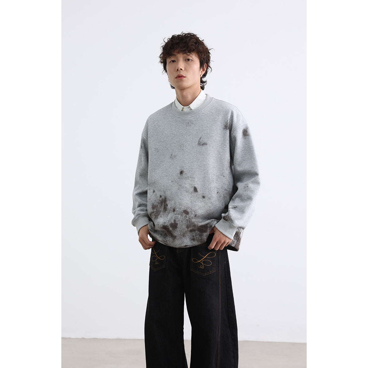 Model wearing a light gray oversized crewneck sweatshirt with dark distressed marks and black wide-leg jeans.