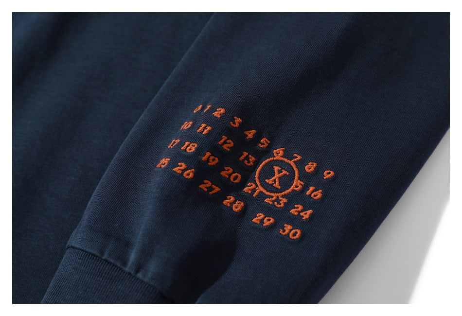 Close-up of an orange numbered embroidery motif on the sleeve of a dark navy shirt.
