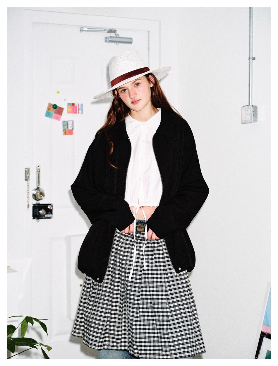 Model wearing a black collared zip jacket over a white blouse and gingham skirt.