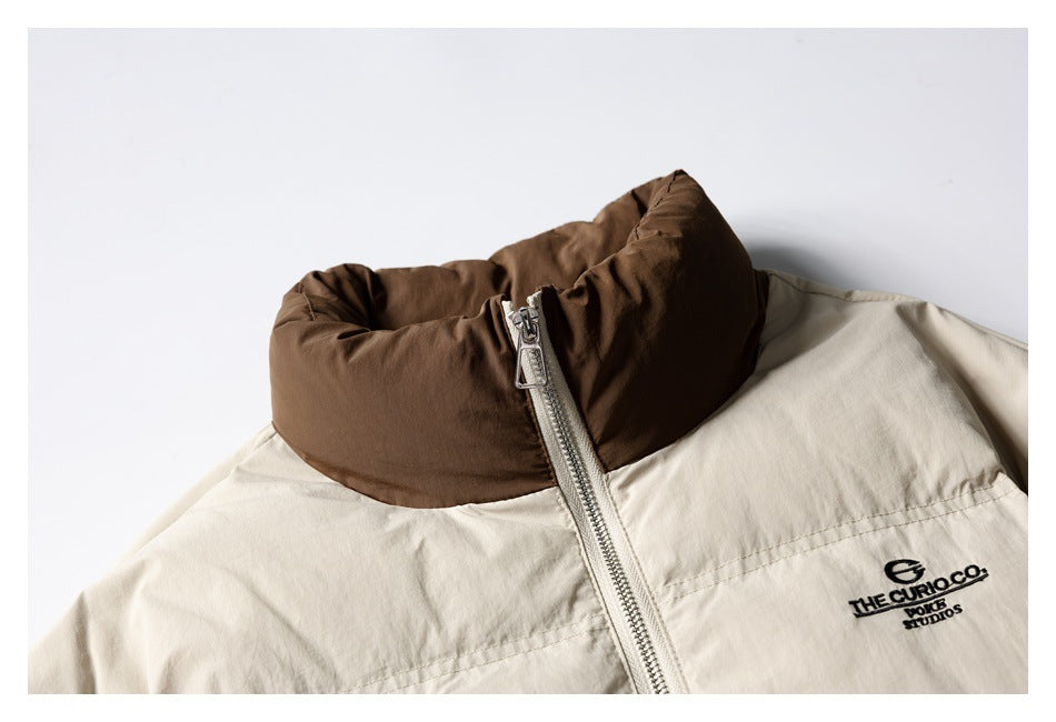 Close-up of a cream jacket with a brown padded collar, silver zipper and black chest embroidery.