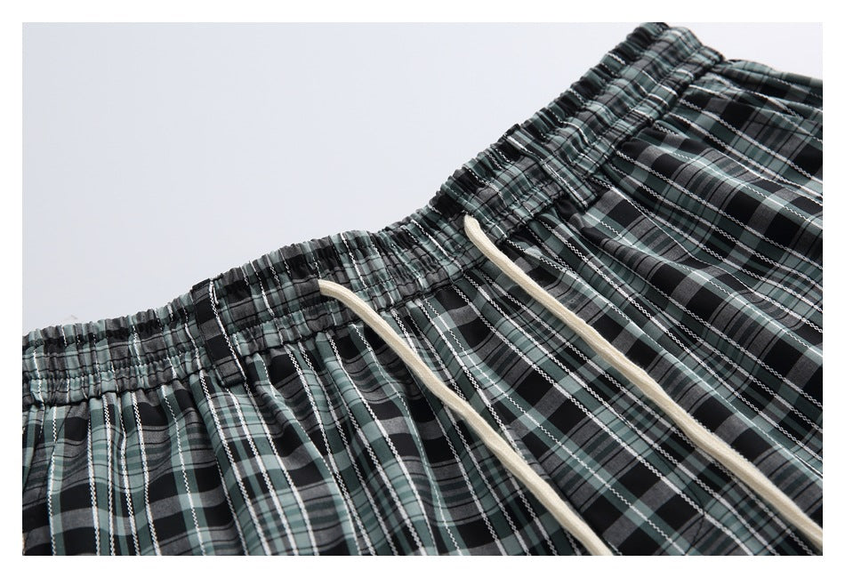 Close-up of the elastic waistband and cream drawstrings on black, gray, and muted green plaid shorts.