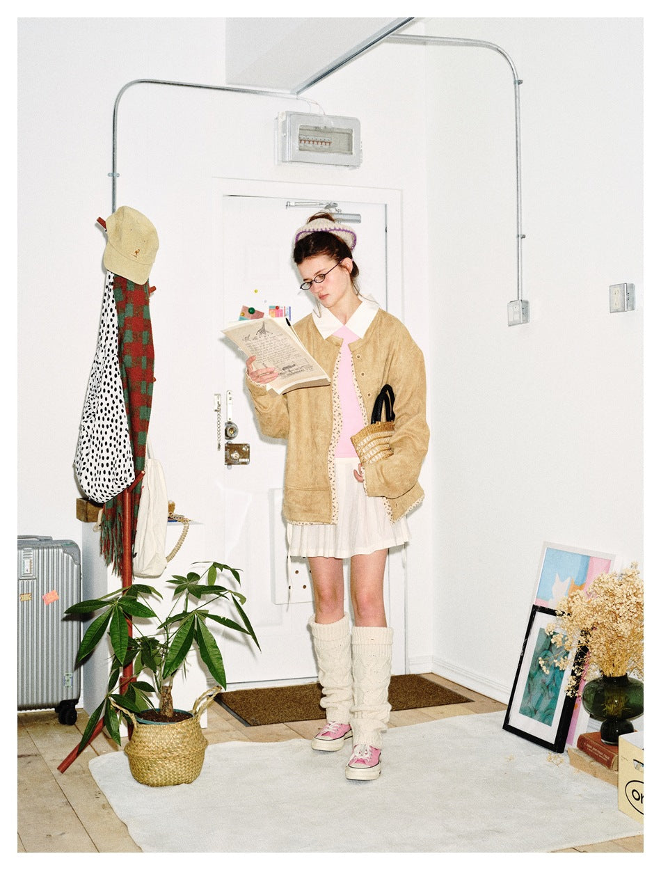 Model reading a paper while wearing a camel collarless jacket with floral trim over a pink top and white skirt