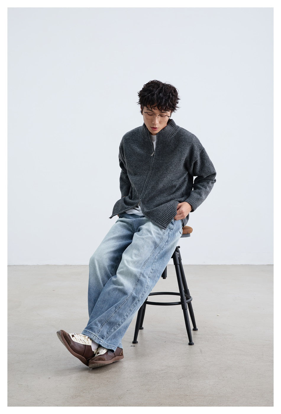 Seated model wearing a charcoal gray zip-front cardigan with ribbed trim and light-wash jeans.