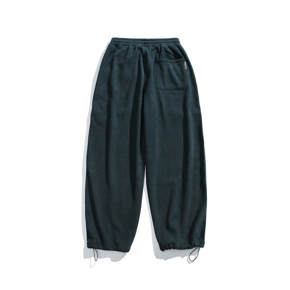 Back view of dark teal loose-fit pants with an elastic waist, one patch pocket, and elastic cuffs with hanging loops.