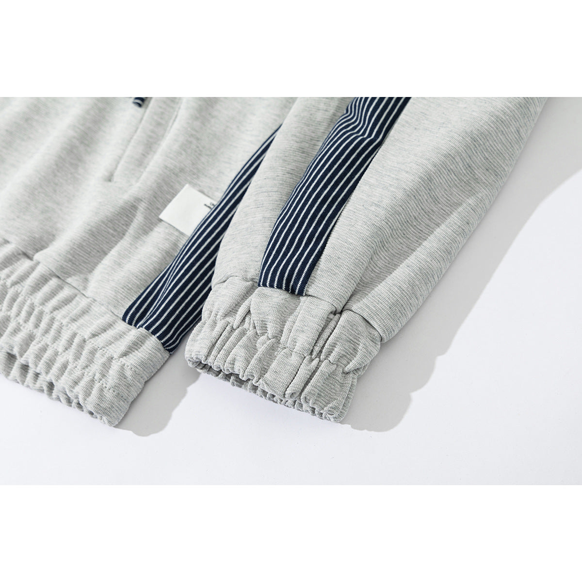 Close-up of light gray jacket sleeves with navy-and-white striped panels and gathered cuffs.