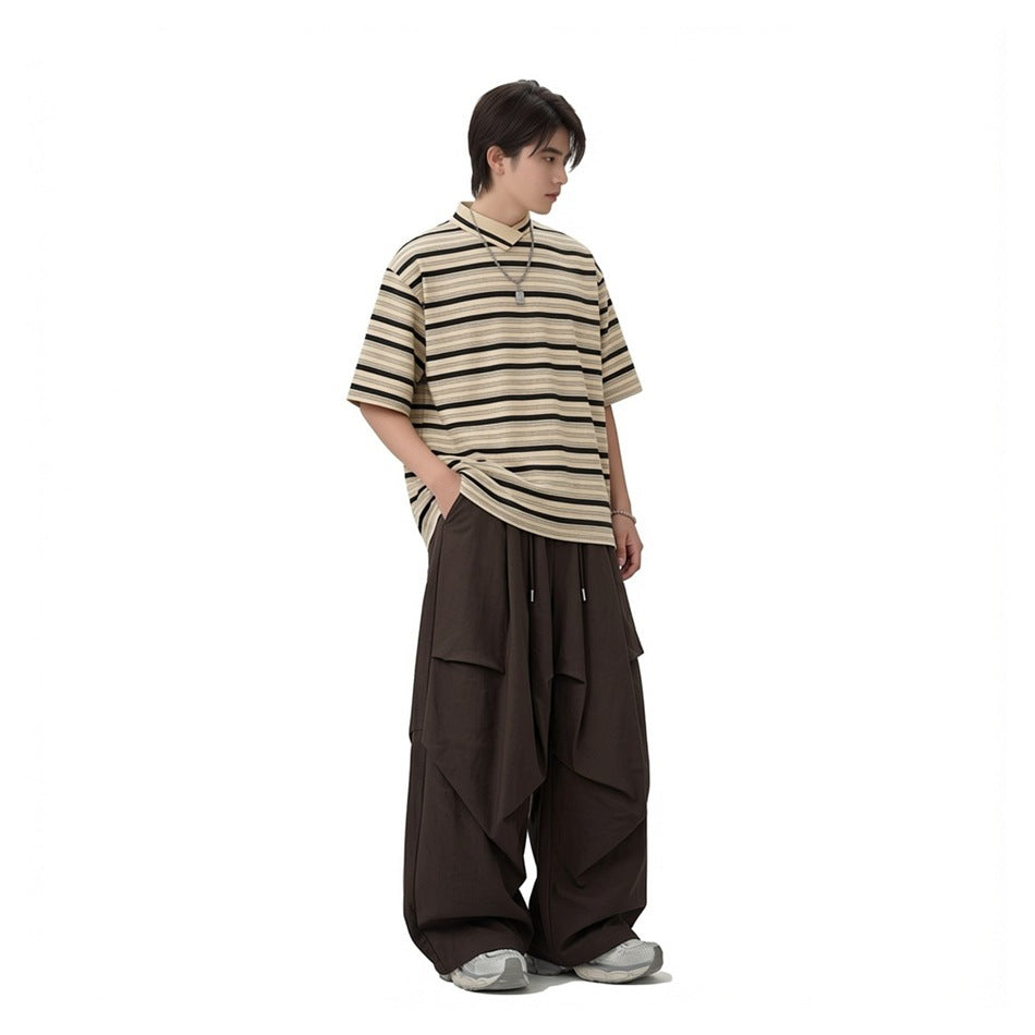 Model wearing a beige and black striped oversized collared T-shirt with dark wide-leg pants.