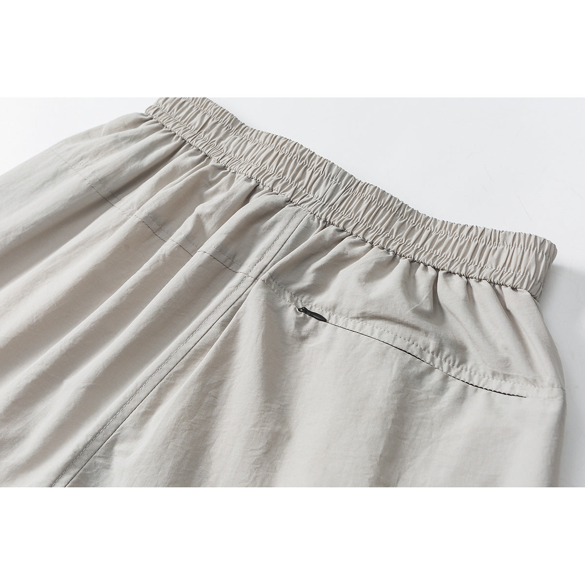 Close-up of the back of light gray trousers, showing a gathered waistband and a small zip pocket.
