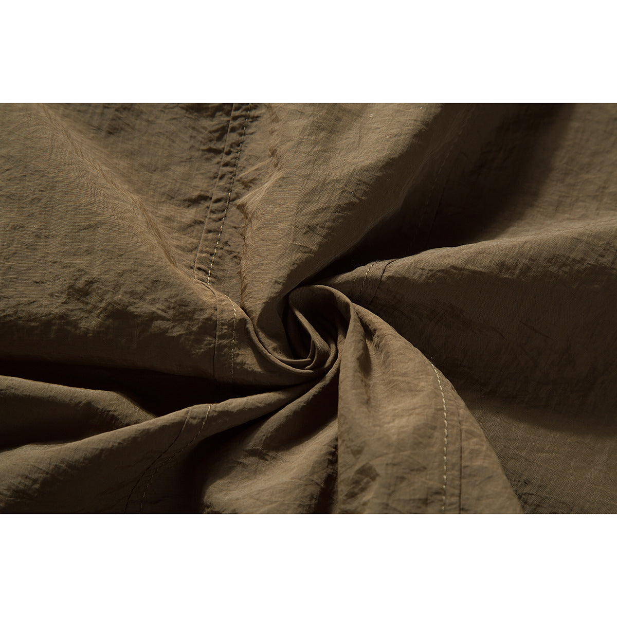Close-up of the olive-brown shirt fabric and stitched construction, gathered into folds.