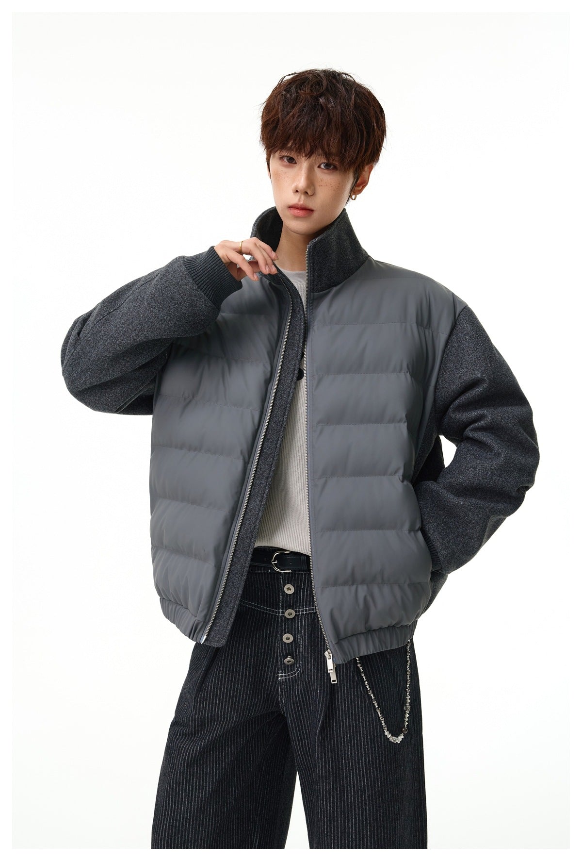 Model wearing a charcoal gray hybrid jacket with a quilted front, textured sleeves, and a high collar.