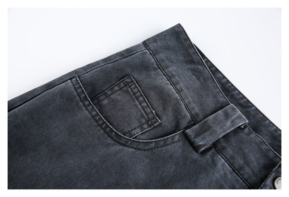 Close-up of dark charcoal jeans showing a small front pocket, curved pocket seam, belt loop and waistband.