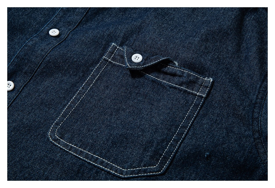 Close-up of a dark indigo shirt chest pocket with contrast stitching and white buttons.