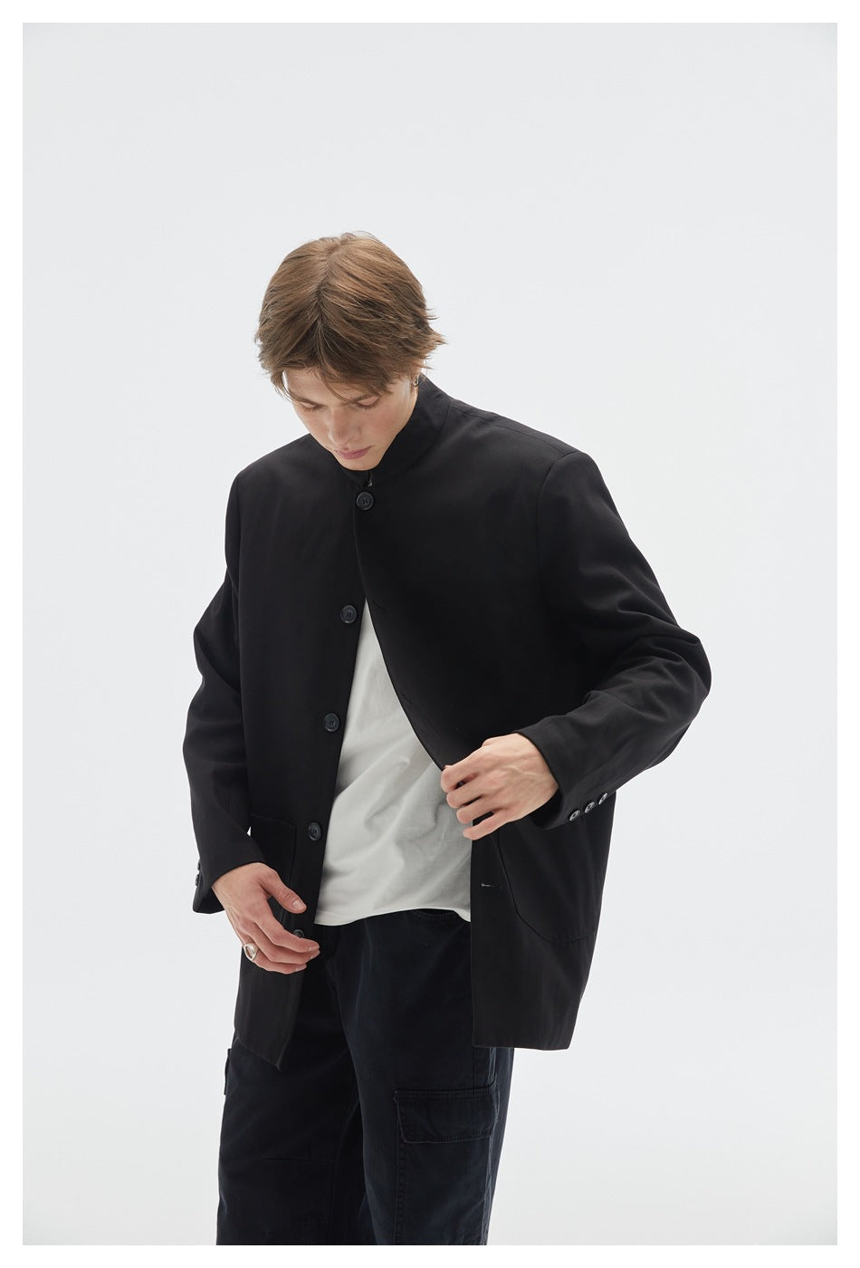 Model looking down wearing a black button-front stand-collar jacket over a white tee, close three-quarter view