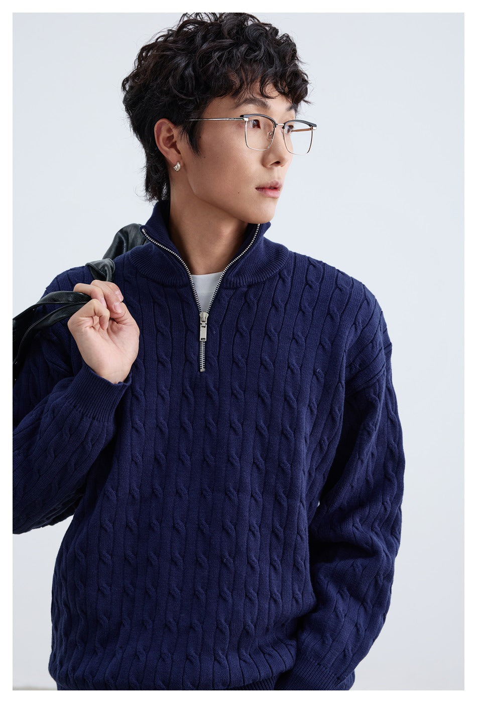 Close view of a model wearing a navy cable-knit sweater, highlighting its raised knit pattern and short zipper.
