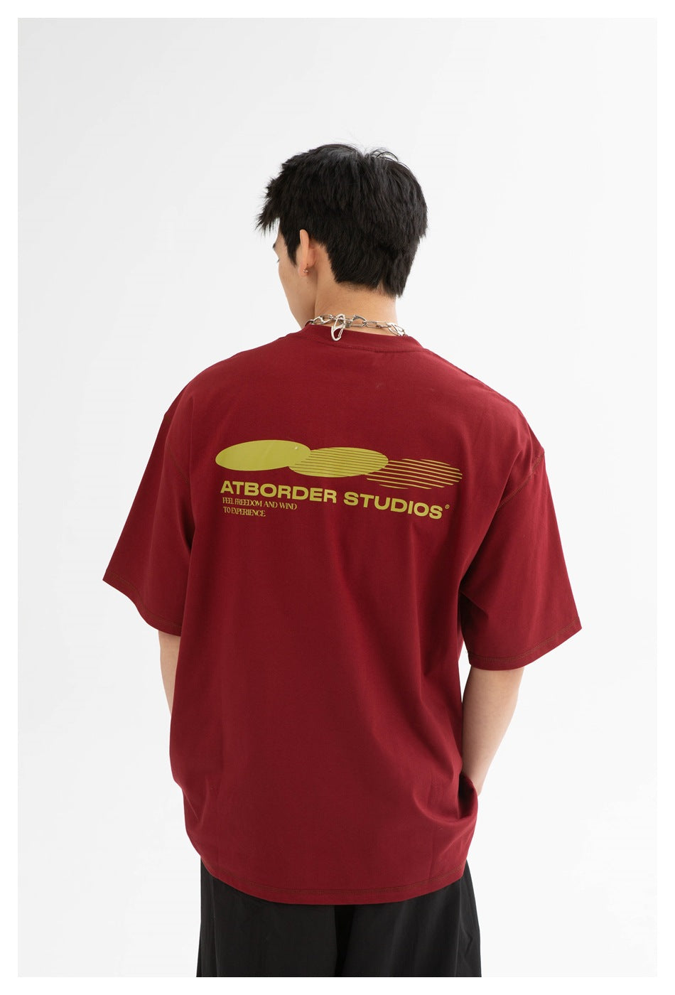 Back view of a model wearing an oversized burgundy T-shirt with a large yellow-green graphic and text.