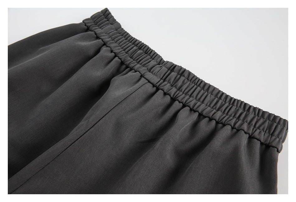 Close-up of charcoal trousers showing a gathered elastic waistband and pleated fabric.