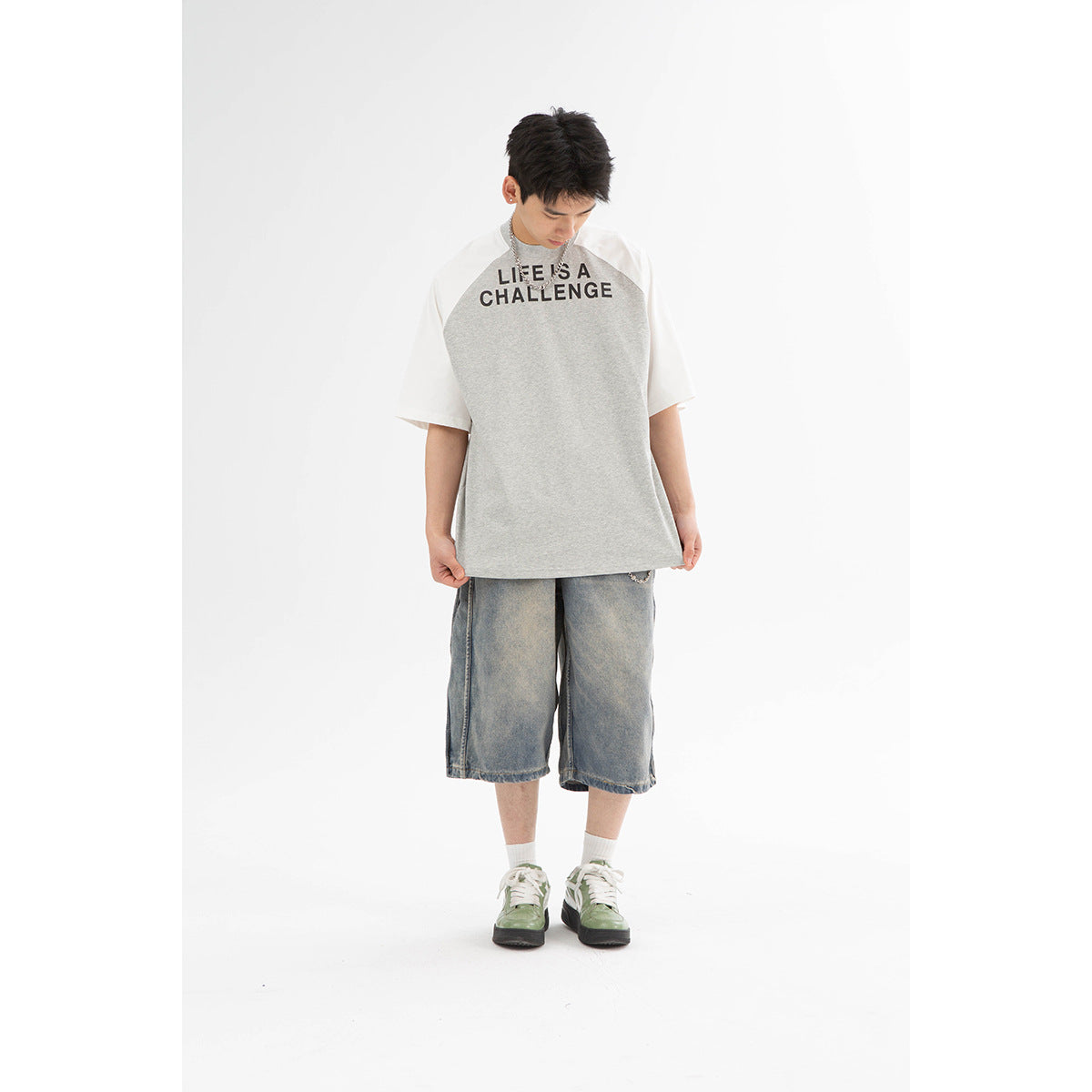 Front view of a model wearing a gray-and-white raglan T-shirt with black lettering and loose washed denim shorts.