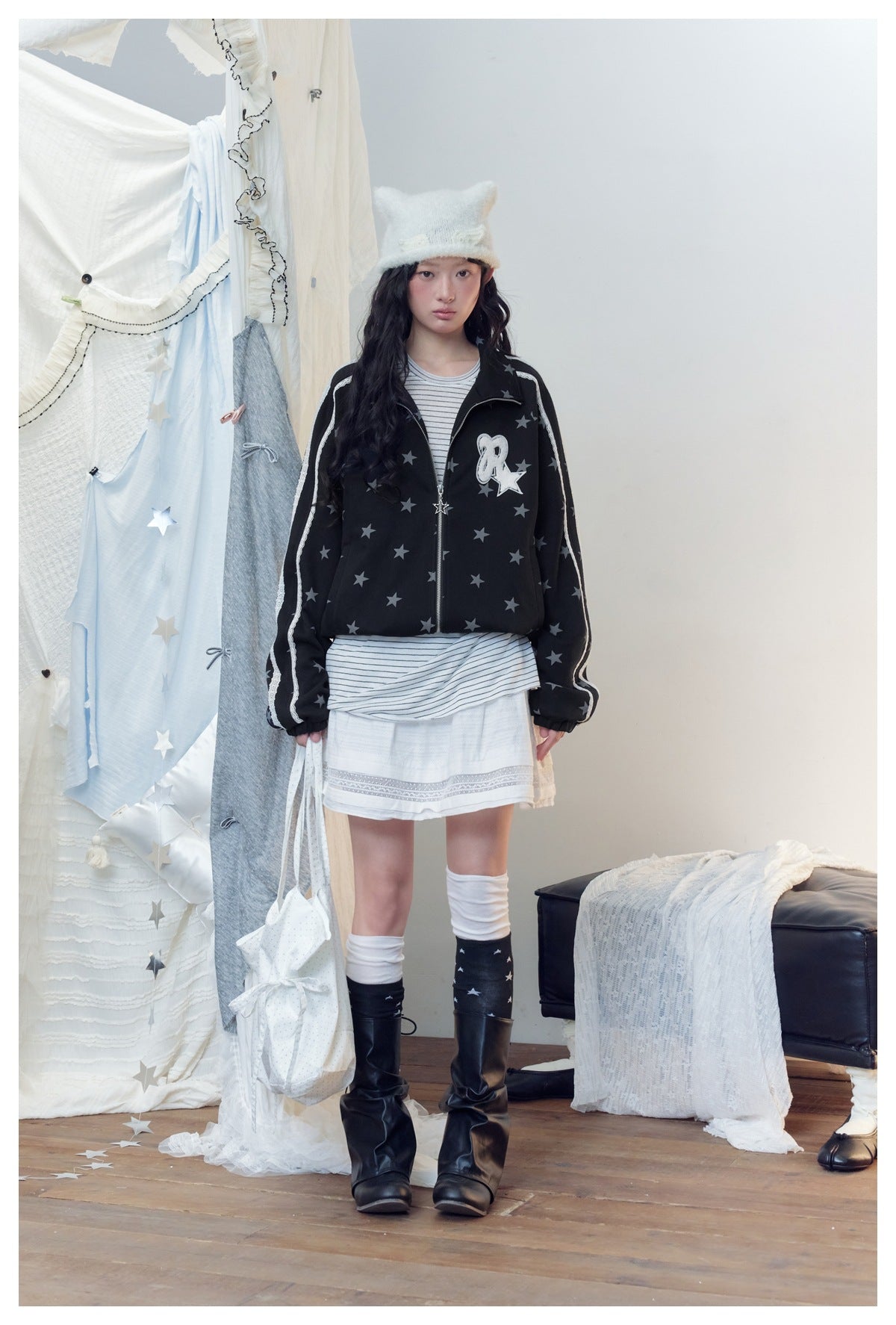 Model wearing the black star-print zip jacket open over a striped top, white skirt, knee socks and black boots