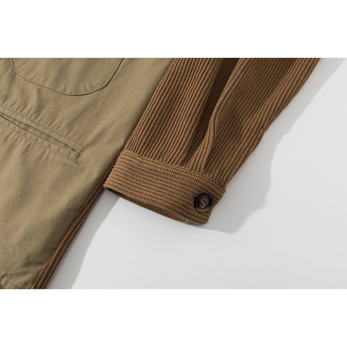 Close-up of a tan jacket’s ribbed sleeve and button cuff beside a chest pocket.