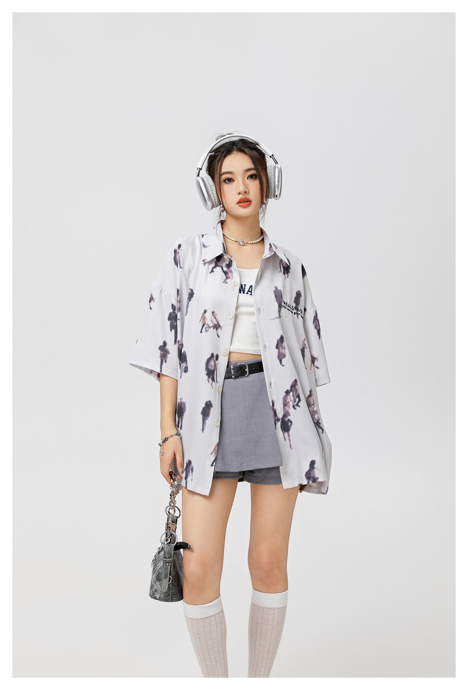 Model wearing a pale gray scattered-people-print shirt, shown with headphones and a small shoulder bag.