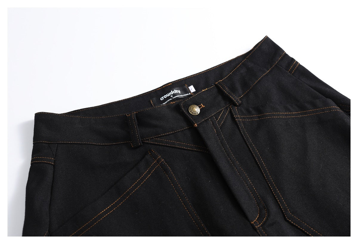 Close-up of black jeans showing the front waistband, button, belt loops, and orange stitching.