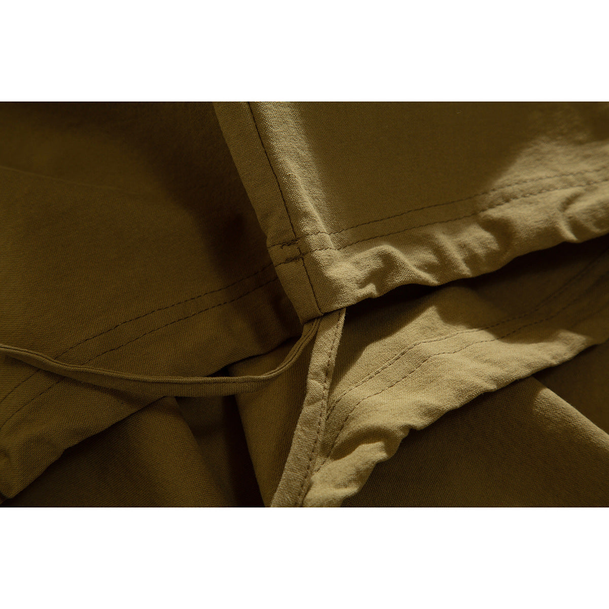 Close-up of the tan shirt's stitched hem and folded fabric.