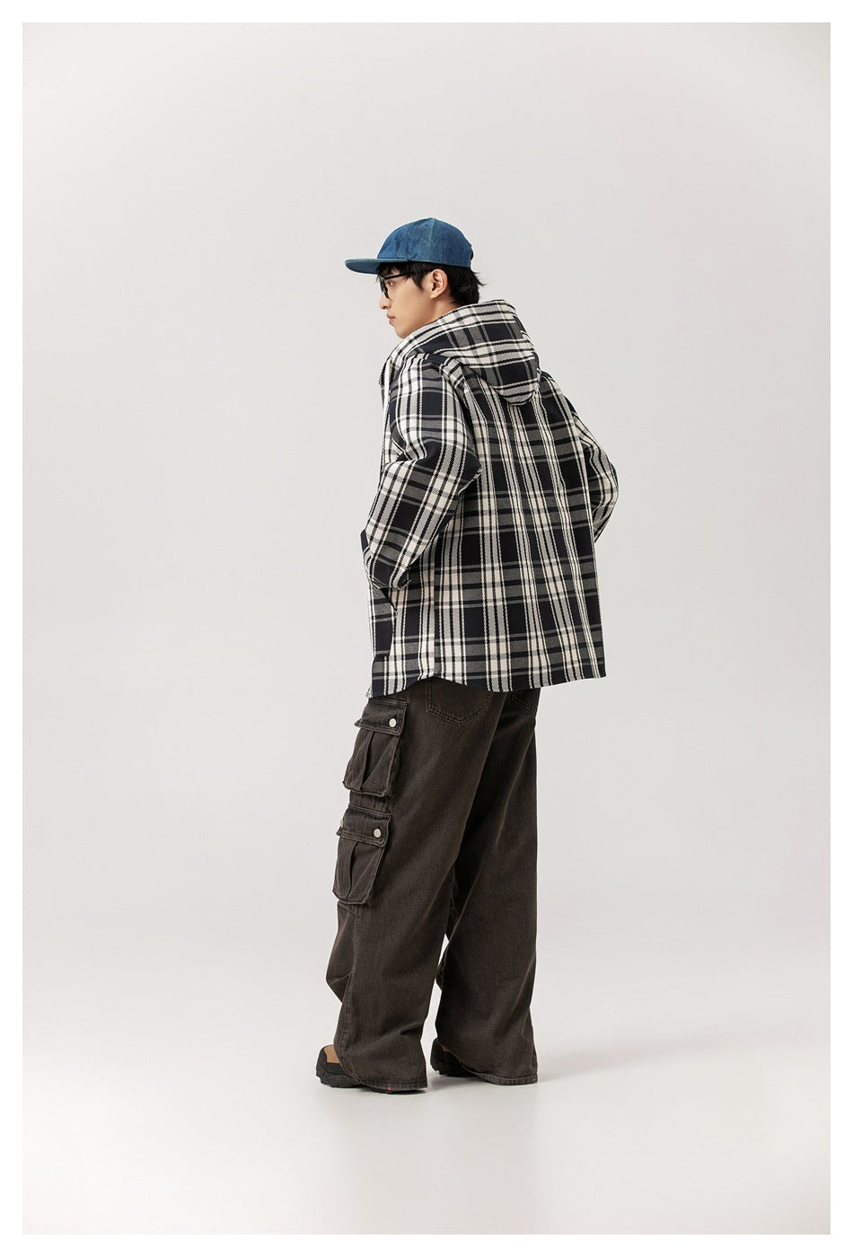 Model seen from the back in the plaid hooded jacket with a blue cap and brown cargo pants