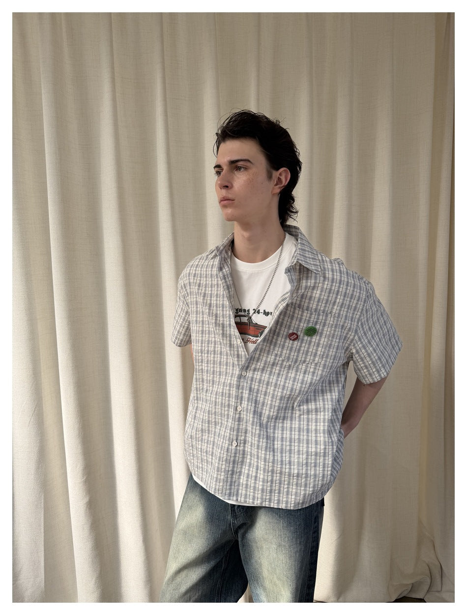 Angled view of a model wearing a white and blue plaid short-sleeve button-up shirt.