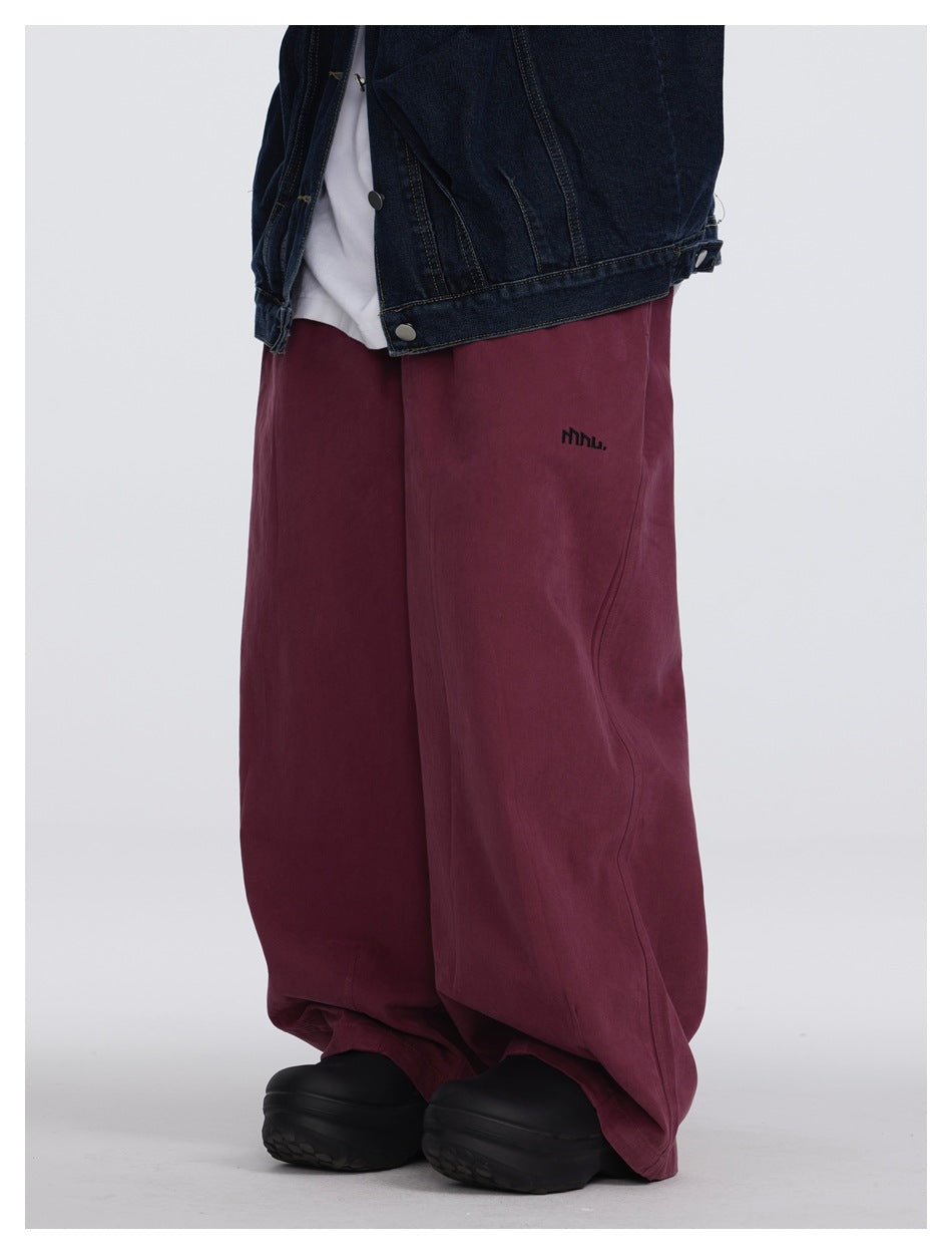 Close angled view of burgundy wide-leg pants worn with a dark denim vest, showing the leg shape and small garment mark.